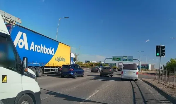 A curtain-sided lorry, vans and cars waiting at the lights on a busy junction