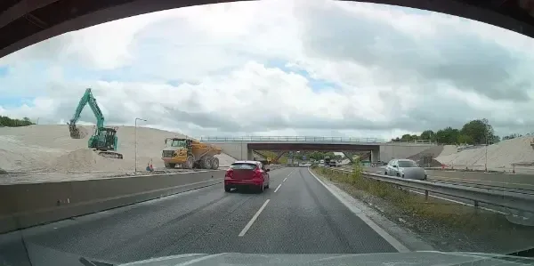 Earthworks, a digger and a dumper beside a dual carriageway, with a new bridge being built